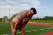 © we.bond.creations - Exhausted male athlete resting on a stadium track, catching breath after an intense workout, embodying dedication and perseverance in fitness