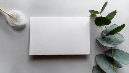 Poster - Blank card resting on a light grey surface with a feather and a eucalyptus branch. Simple design with natural accents. Copy space for your text. Calm and peaceful scene.