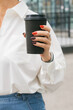 © satura_ - Woman holding takeaway coffee cup outdoors. Morning refreshment, city lifestyle and casual business routine.