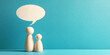 © Inspire Shots Hub - Two wooden figures stand before a blank speech bubble against a teal background, symbolizing communication, dialogue, or family interaction, suitable for communication or family concepts