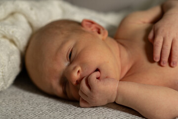Aufkleber - Baby lying on soft blanket, peacefully dreaming with fingers in mouth in warm indoor setting during morning light