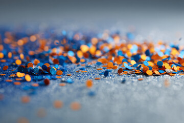 Poster - Blue and orange confetti scattered on a glittery surface, creating a festive and celebratory mood, ideal for holiday or party backgrounds