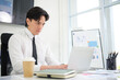 © wattana - Focused young man in formal attire using a laptop at a modern office desk with coffee and documents.
