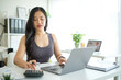 © wattana - Young woman using a calculator and laptop, managing financial documents in a bright workspace.