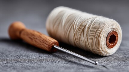 Poster - Wooden needle and a spool of thread are on a grey surface. The needle is pointed and the thread is white