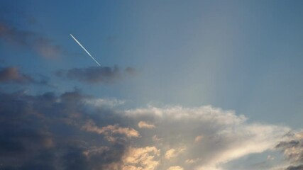 Poster - Sunset with vibrant clouds in shades of yellow, orange and blue illuminated by golden sun rays. A serene moment capturing nature beauty and tranquility for relaxation. The plane flies leaving a trail