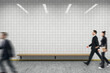 © Who is Danny - Modern tiled wall background with blurred business people walking past wooden bench under bright ceiling lights in creative interior design space.
