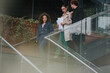 © qunica.com - Three business professionals walking down glass stairs while discussing documents, representing teamwork and communication in a corporate environment.