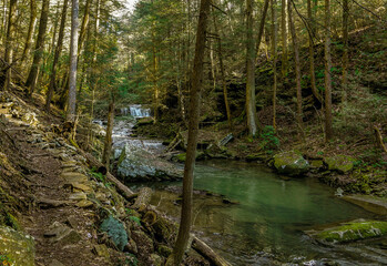 Blue Hole Falls is visible in the background in this image of a river flowing through the Grundy Forest in South Cumberland State Park in Tennessee. A hiking trail runs along the river. Horizontal