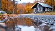 A quaint cabin nestled in a vibrant autumn forest, serene reflection in a puddle on a gravel path, and peaceful countryside setting.