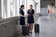© NVB Stocker - Portrait two Cabin crew or air hostess in airport. Cabin crew, air hostess working in airplane. Service mind. Asian stewardess with suitcase at modern airport terminal. flight attendant