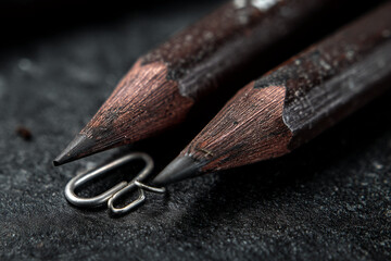 Poster - Close-up of two dark brown pencils, graphite tips visible, resting on dark surface, showcasing texture and detail, symbolic of art, creativity, and writing