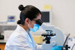 © Anass - Scientist in laboratory setting examining samples through a microscope with protective gear