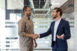 © Liubomir - Two businessmen shake hands in a modern office, smiling warmly during a professional agreement or greeting, with natural light.
