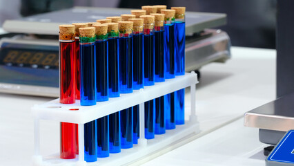 Poster - A row of test tubes with blue and red liquids are lined up on a table in a biological chemistry lab. Analytics medicine pharmaceuticals microbiology concept background