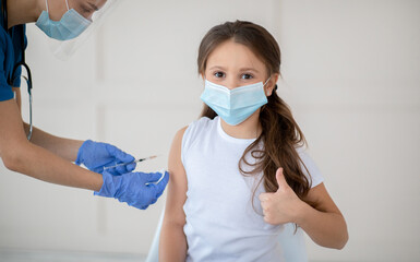 Poster - Little girl in face mask gesturing thumb up while receiving covid-19 vaccine injection at health centre. Cute child approving of coronavirus immunization, being protected against global virus