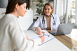 © Moon Safari - Female doctor in lab coat working over laptop on desk while patient writing details on clipboard in hospital