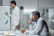 © pressmaster - Scientists are examining and discussing data on whiteboard in laboratory setting, with various equipment visible. One scientist actively writing while another attentively watching