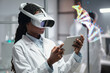 © pressmaster - Female scientist wearing VR headset and using tablet for conducting research in laboratory. DNA model visualization in background, creating tech-savvy working environment