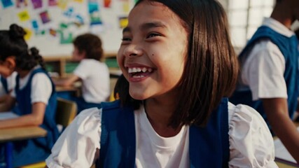 A cheerful girl in a classroom smiles at the camera. The video captures a close-up, eye-level angle, highlighting her joy and the vibrant learning environment.