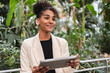 © Westend61 - Smiling woman holding a tablet in an airport surrounded by greenery
