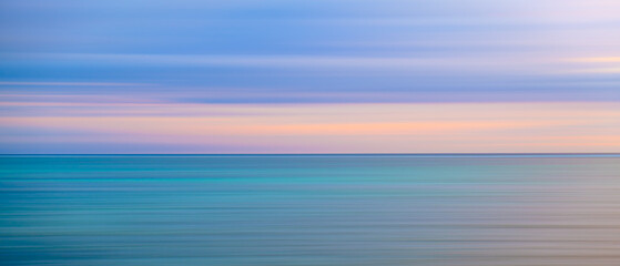 Poster - The image is a blurry depiction of a calm ocean with a pink sky. The water appears to be a deep blue color, and the sky is a soft pink hue. Concept of tranquility and serenity
