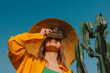 © VISTA by Westend61 - Stylish woman on vacation photographing with a vintage camera near a cactus