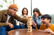 © BJ Day Stock - Happy asian diverse group friends playing with wooden building blocks at home office sitting at the table enjoying time together. Office leisure and board games concept.