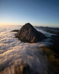 Wall Mural - Majestic mountain peak rising above a sea of clouds at dawn creating a serene and breathtaking landscape aerial view with a clear blue sky and soft golden light