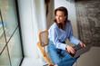 © sepy - Attractive brunette haired woman sitting on a chair by the window in her modern house and using notebook