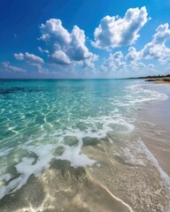 Poster - Serene turquoise ocean meeting sandy shore under a bright blue sky with fluffy white clouds creating a peaceful tropical beach scene with crystal clear water