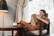 © SHOTPRIME STUDIO - Relaxed young woman in stylish brown outfit enjoying reading on a tablet in a cozy indoor setting with warm lighting