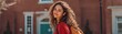 © Tichakon - A woman with curly hair smiles at the camera, and the image is captured with a backdrop of a building