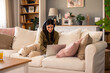 © Dorde - Young Woman Wearing Headphones Using Laptop in a Cozy Living Room with Cushions and Decor