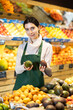© JackF - Young woman seller in apron offers fresh avocado in vegetable shop