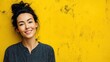 © Newleks - Smiling professional young woman with dark hair pulled back, standing near bright yellow textured wall, conveying positive workplace energy