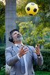 © Pix4Ads - Indian corporate man playing football while listening music through headphone at park. Asian Business man fun at park