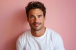 © Olya - young man with curly hair wearing a plain white t-shirt against a light pink background, casual and relaxed posture