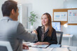 © amnaj - Two Asian businesspeople shaking hands in a modern office, celebrating the successful closing of a deal and fostering a strong partnership
