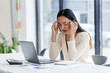 © amnaj - Young professional woman feeling tired and having a bad headache after working on computer for long hours in modern office
