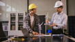 © NanSan - Two Asian businessmen wearing engineer hats table, discussing solar panels and wind turbines. They plan environmental projects, focusing on solar energy solutions and renewable energy installations