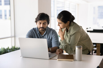 Two Indian teammates analyze data, working on joint project using modern laptop, look at spreadsheets, reports, or analytics, making decisions, solve work-related matters, generate business strategy