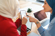 © Studio Marmellata - Two women in hijabs are collaborating on a project. They're using a phone to check their schedule and plan their next steps, ensuring they stay on track with their goals.