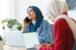 © Studio Marmellata - Two women in hijabs are working together. One is on a call, possibly discussing a project, while the other focuses on her laptop. They're collaborating to achieve a common goal.