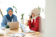 © Studio Marmellata - Two women are working together in a bright office. One is on a call, possibly discussing a project, while the other focuses on her laptop. They're collaborating to achieve their work goals.
