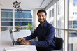 © fizkes - Portrait of successful professional African businessman, office employee sitting at table working on laptop in modern boardroom, look at camera, feel happy and proud with achievements, career growth