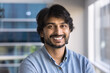 © fizkes - Head shot portrait of happy Indian businessman, company head or executive manager dressed in casual shirt posing for camera standing alone in modern workplace, profile picture. Professionalism, career