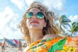 © Amanda - Woman enjoying summer beach day with sunglasses and vibrant floral shirt, relaxing in sunshine with blurred beach background and palm trees.