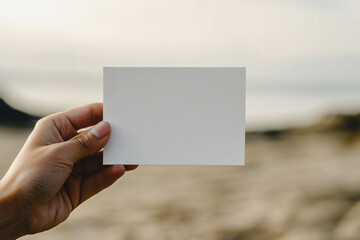 Aufkleber - Hand holding blank white card, blurred beach background.