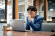 © bongkarn - Blue suit asian man is looking intently at his laptop on table while sitting in cafe or coffee shop.